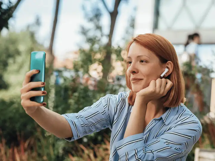 Young woman wearing an earbud smiling during a video call outdoors
